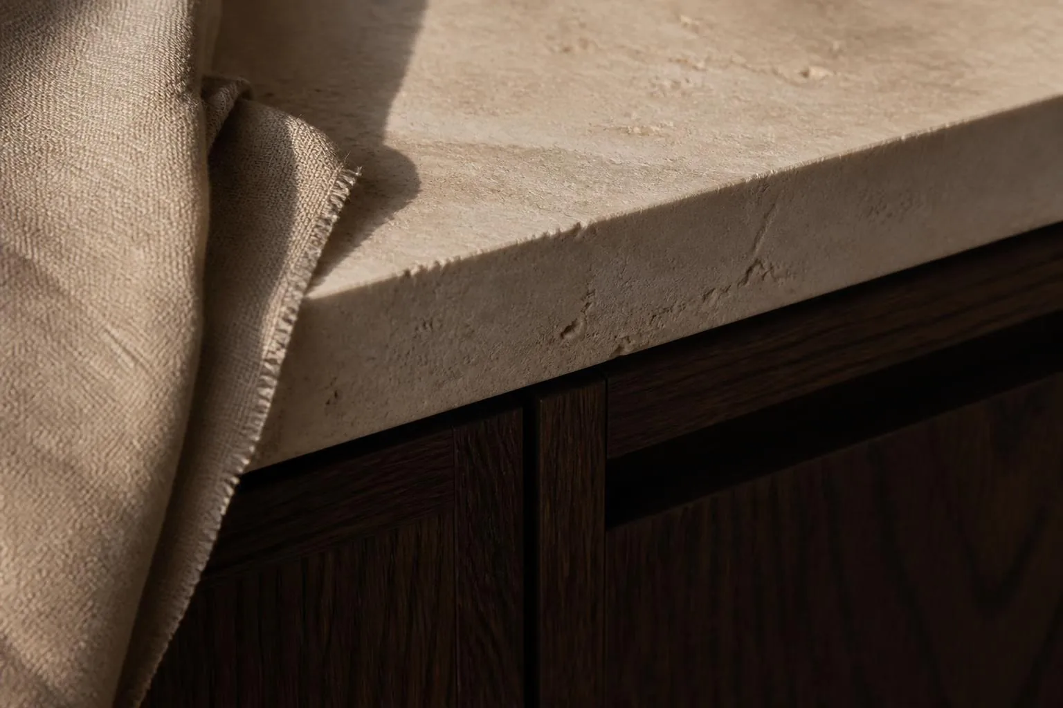 Detalle del encuentro entre una cubierta de piedra natural, un mueble de madera oscura y un textil de lino